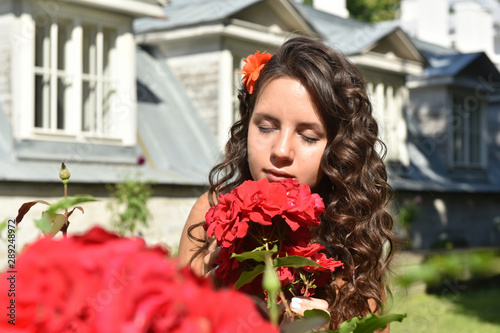 beautiful girl with curls next to red roses in the garden photo