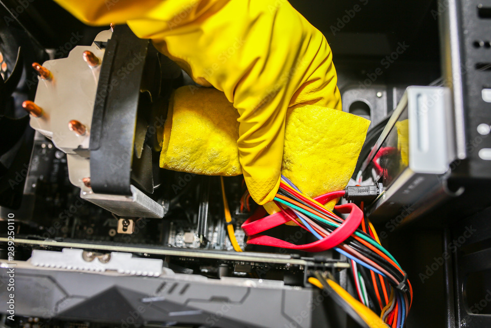 Fototapeta premium Inside details of the personal computer. Man is cleaning wires in yellow gloves. Motherboard and video card in the dust. Broken PC.