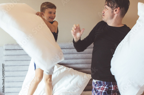 Happy boy and his father pillow fighting in the bedroom.