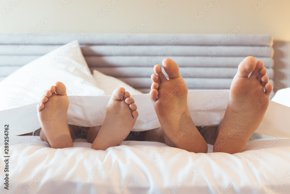 Feet of father and child under bed sheet.