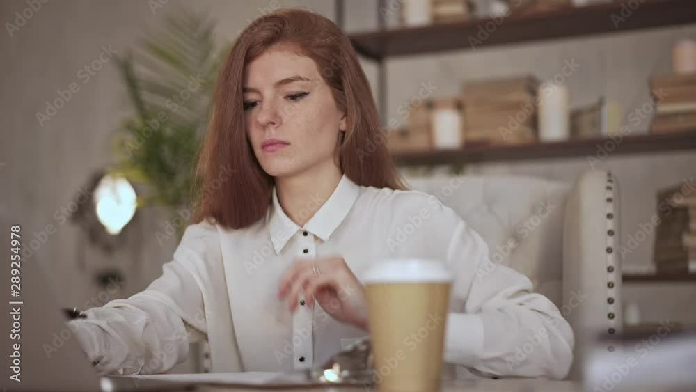 Serious young businesswoman with long red hair typing on laptop in modern office. Slider slow motion medium shot Serious young businesswoman with long red hair typing on laptop in modern office. Slider slow motion medium shot