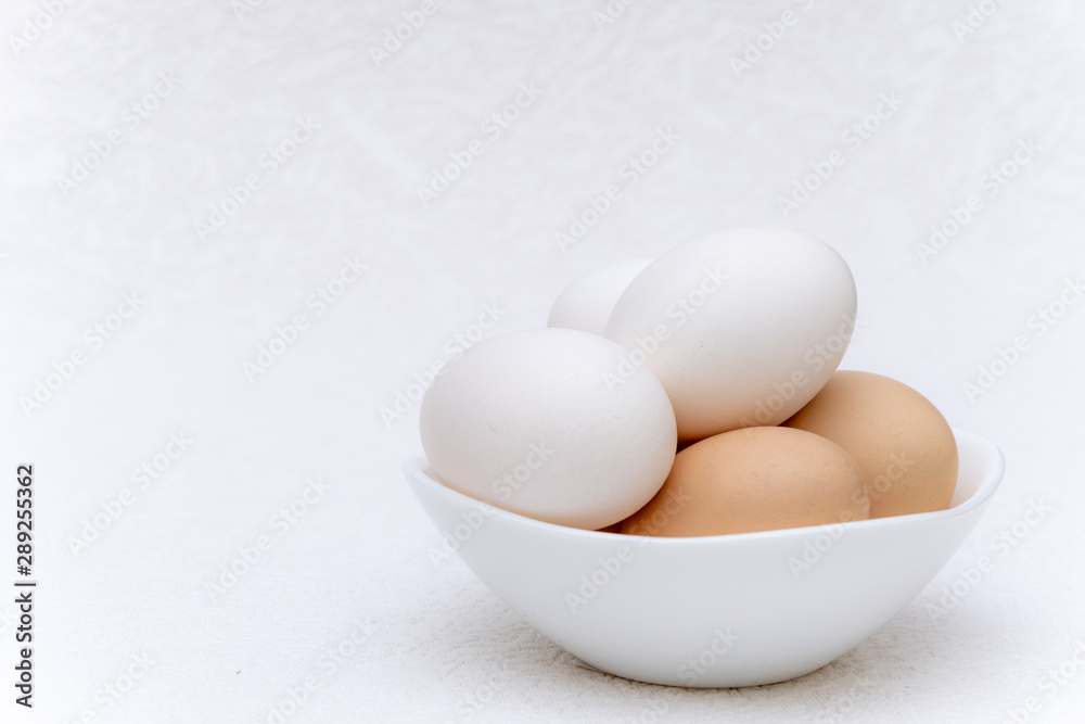 Whole white and brown eggs in a white bowl on a white surface Whole white and brown eggs in a white bowl on a white surface