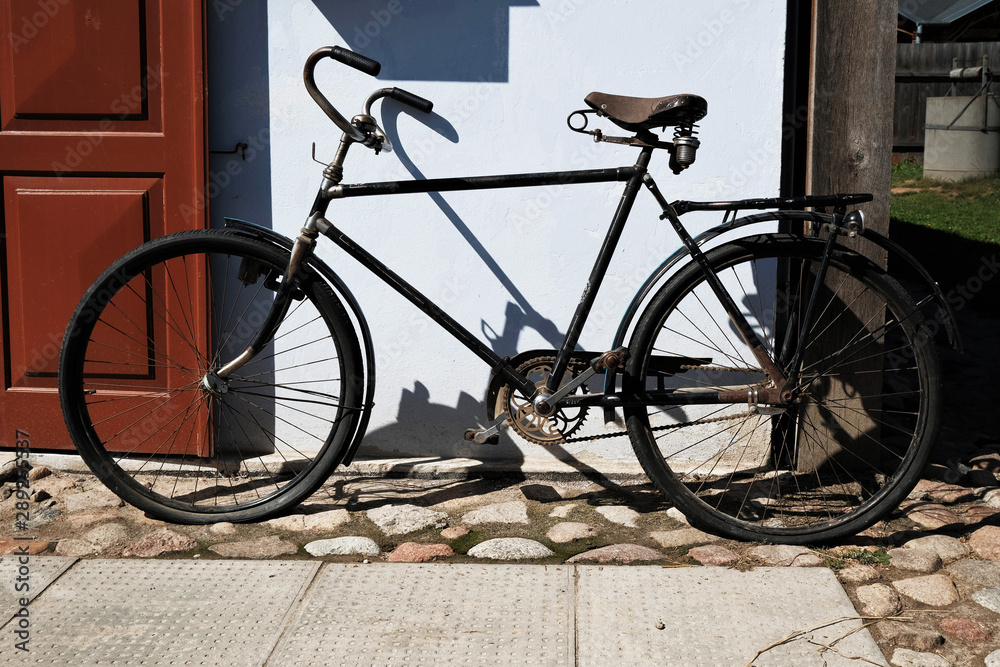 vintage black bicycle parked outside old house with wooden door, casting strong shadows on white wall
