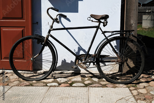 vintage black bicycle parked outside old house with wooden door, casting strong shadows on white wall