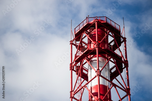 Red and white chemical plant pipe throws harmful poisonous smoke into clear blue sky with copy space. Concept of greenhouse effect and air pollution due to fuel combustion and chemical production.