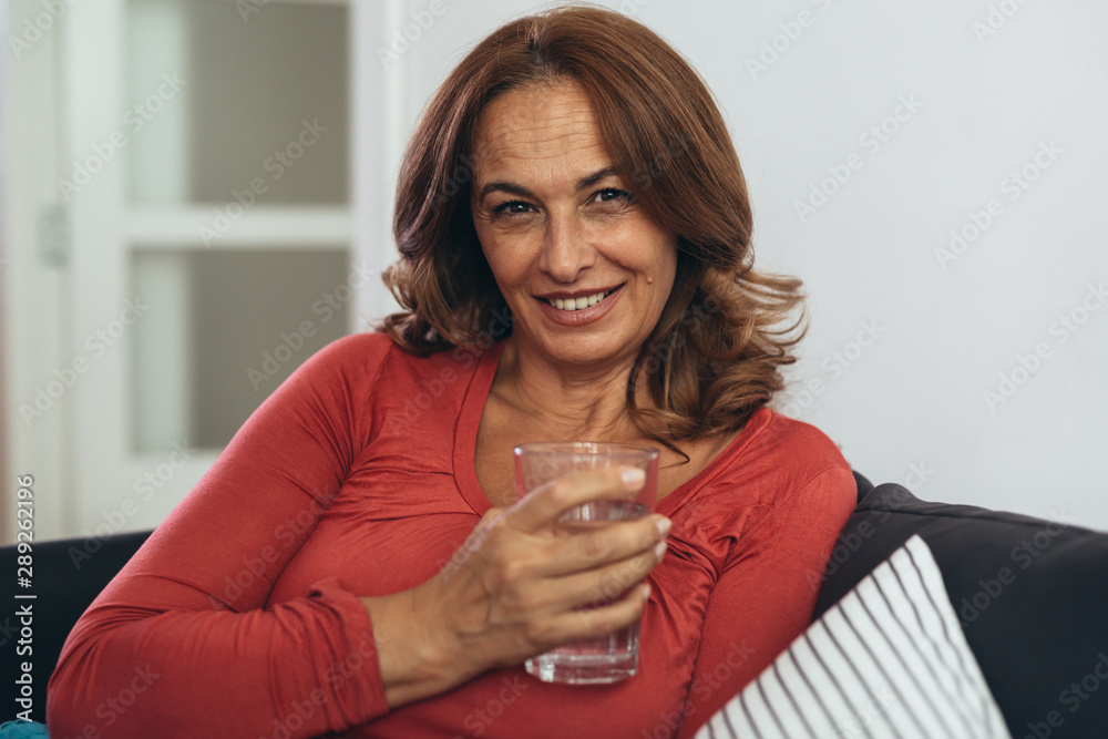 middle aged woman sitting sofa and drinking water at her home middle aged woman sitting sofa and drinking water at her home