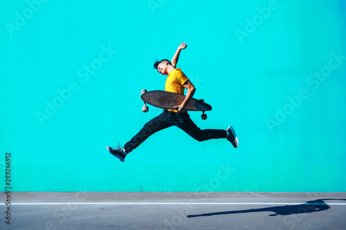 Skater Boy jumping with longboard in the colorful street photo