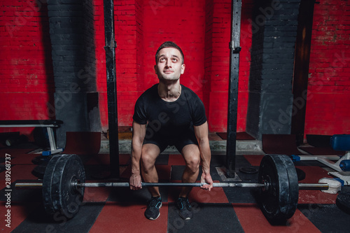 Young athlete dressed in black t-shirt. During this time, he trains crossfit to the gym. At the same time, it raises the bar with maximum effort.