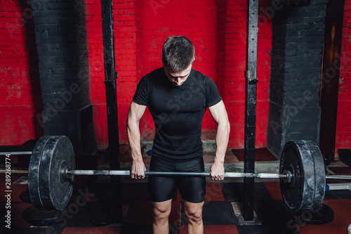 Young athlete dressed in black t-shirt. During this time, he trains crossfit to the gym. At the same time, it raises the bar with maximum effort.