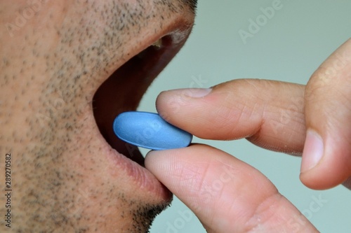 Hand of man holding blue pill. Closeup of a man taking blue medicine pill. Mouth view, illness. Medicine concept of viagra, medication for stomach, erection, sleeping, digestive or drugs photo