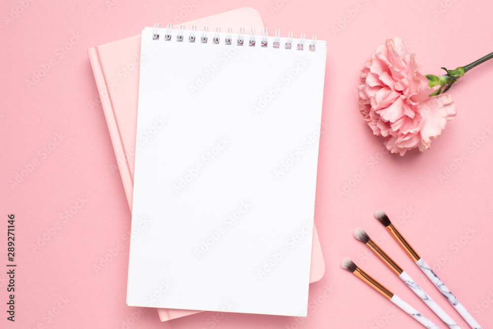 White and pink notebook with carnation flower and make up brushes on a pink background