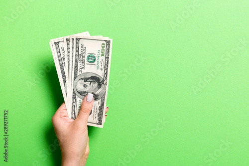 Female hand holding a bundle of money on colorful background. Top view of one hundred dollar banknotes. Salary concept with empty space for your design