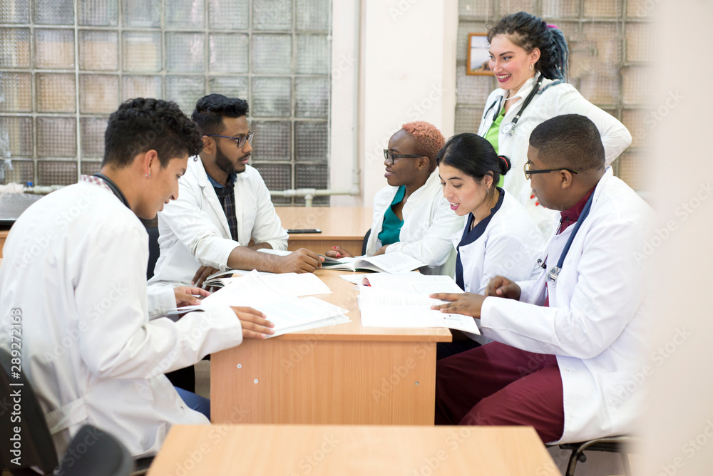a group of young people of mixed race. Doctors in white coats sit at a table in the hospital's office, discuss medical issues and topics.
