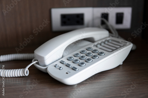 White vintage telephone with grey battoms on a brown table in hotel.