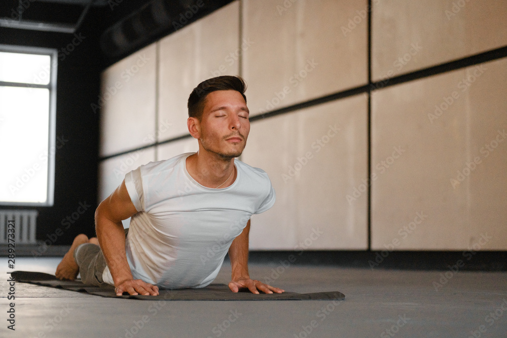 A young man practicing yoga is doing an exercise on cobra, pose of bhujangasana. A young man practicing yoga is doing an exercise on cobra, pose of bhujangasana.