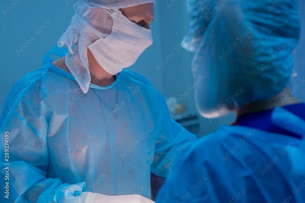Fototapeta premium Children's surgeons perform urological surgery. A man and a woman in a mask, and a blue sterile gown, in the operating room.