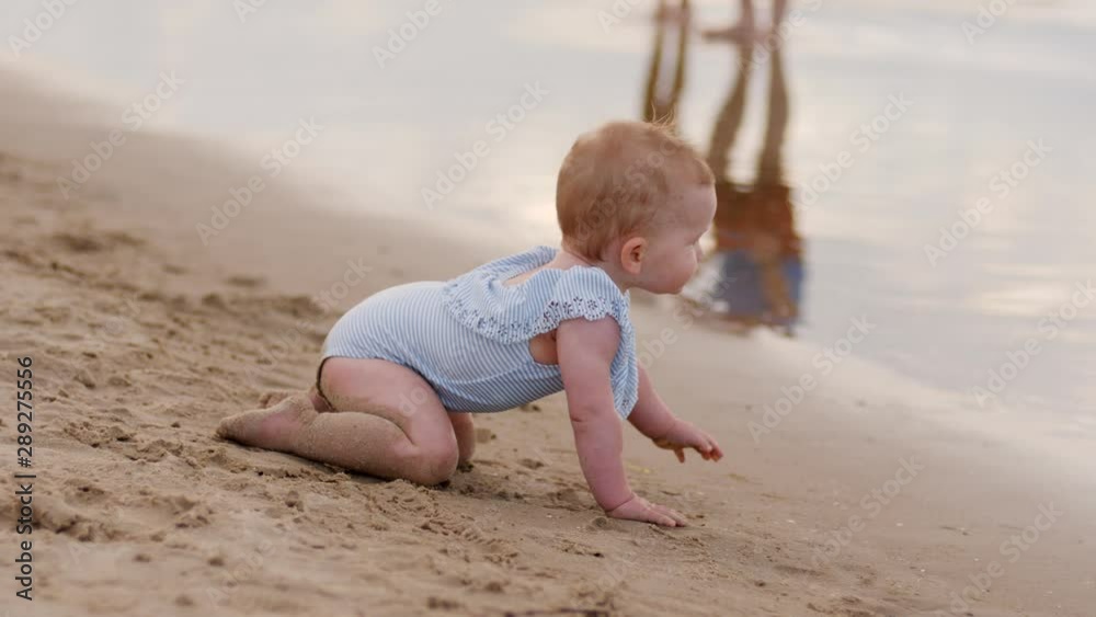 Toddler baby girl crawls into the shallow waterline of Baltic sea sand beach shore enjoy play in water
