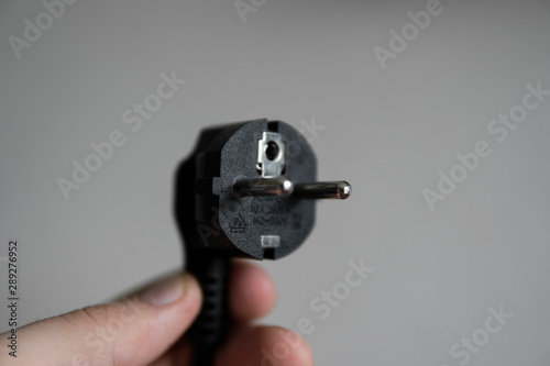 Hand holding black electric plug on a grey background.