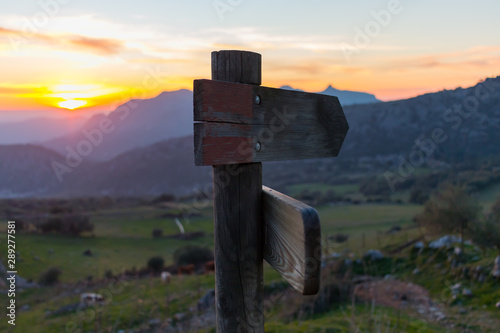 Wooden sign with several directions in front of the mountains at sunset
