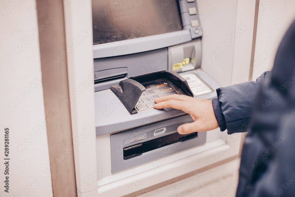 Closeup of male hands using smart phone while typing on ATM, bank machine Closeup of male hands using smart phone while typing on ATM, bank machine