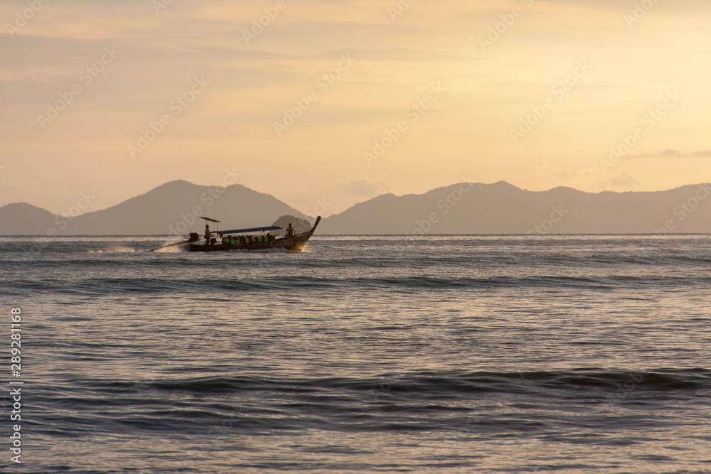 Traditional long boat with tourists sailing by the island in the evening, Thailand. Traditional long boat with tourists sailing by the island in the evening, Thailand.