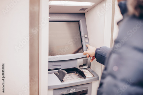 Closeup of male hands using smart phone while typing on ATM, bank machine 