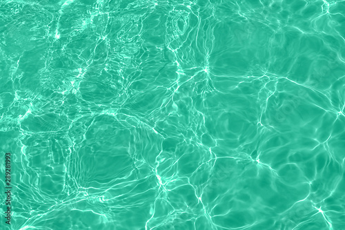 Closeup of calm clear water surface with water splashes in trendy mint color. Swimming pool water texture. Trendy fresh abstract nature background. Color trend concept.