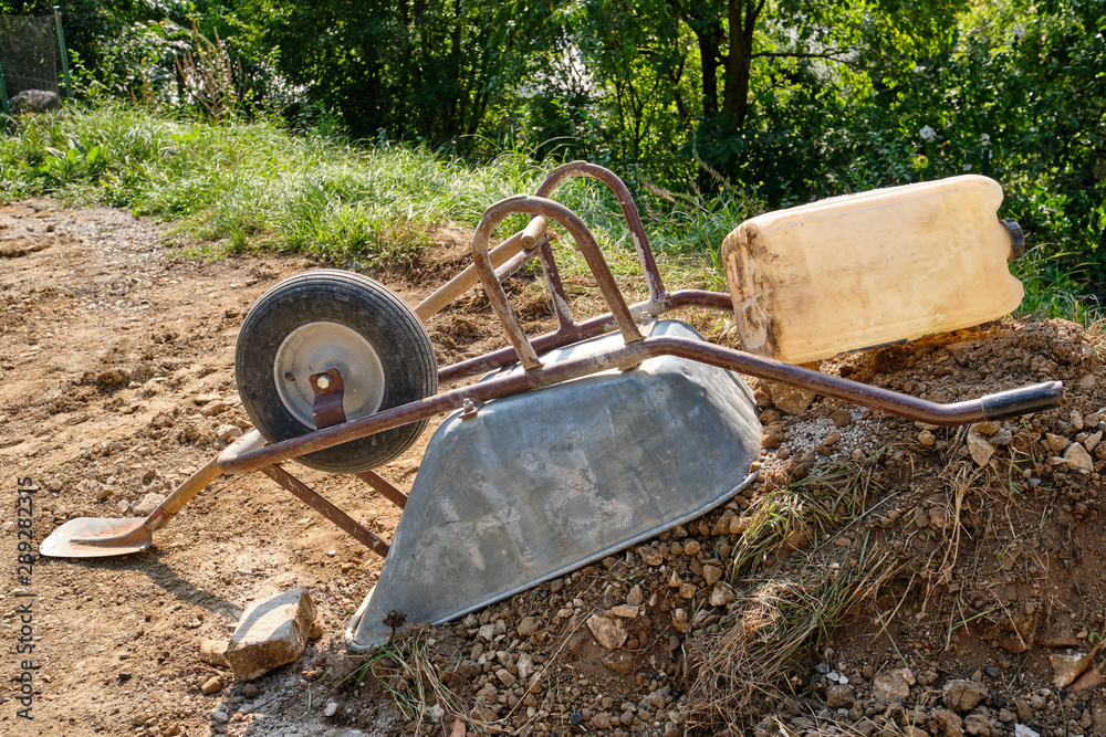 A wheelbarrow is lying upside down on a heap of soil and stones