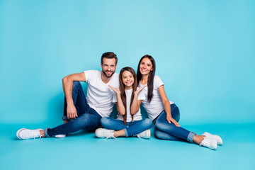 Full length body size photo of family sitting on floor giving you toothy smiles while isolated with blue background