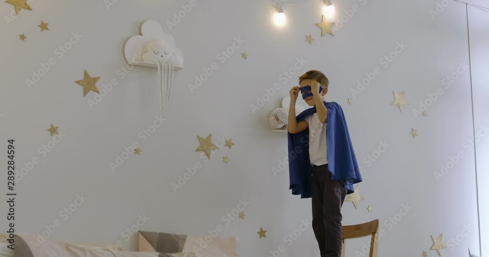 120 FPS SLOW MOTION Cute little Caucasian kid boy wearing blue cape and mask, jumping on a bed, pretending to fly like a superhero. 4K UHD 120 FPS SLOW MOTION Cute little Caucasian kid boy wearing blue cape and mask, jumping on a bed, pretending to fly like a superhero. 4K UHD