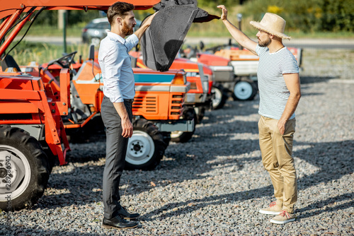 Agronomist choosing a tractor for farming, standing with salesman on the open ground of agricultural shop