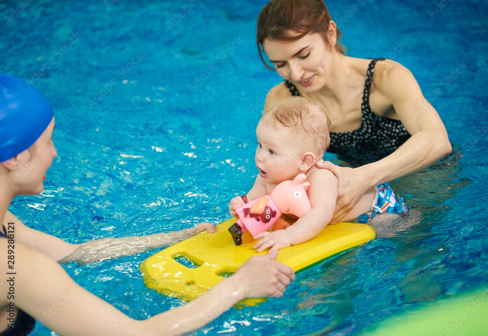 Swimming instructor teaching and helping little baby floating in blue water using auxiliary swimming tools for protection. Family healthy active lifestyle, early development, happy childhood concept