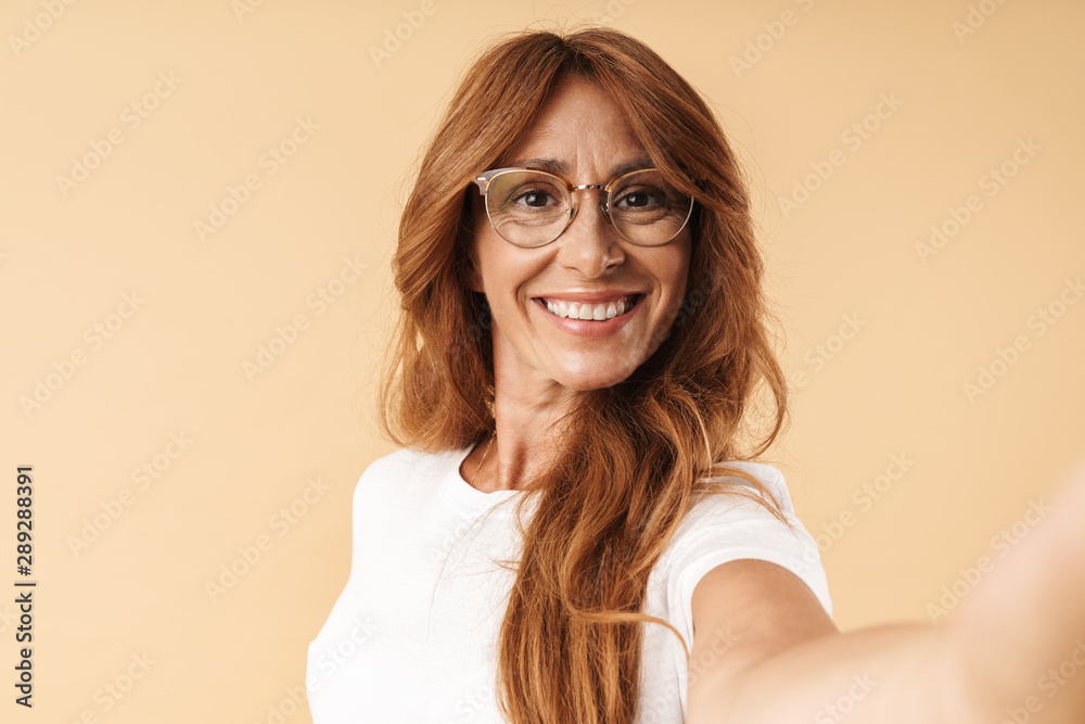 Pleased adult mature beautiful woman posing isolated over beige background  take selfie by camera. Stock Photo | Adobe Stock