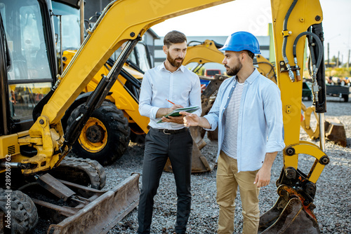 Builder choosing heavy machinery for construction, talking with a sales consultant on the open ground of a shop with special vehicles