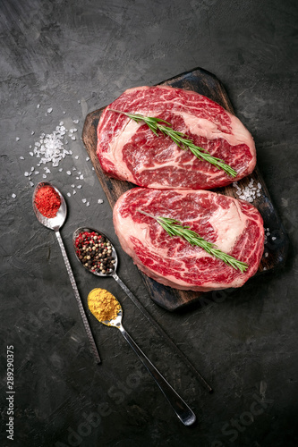Two raw rib eye steak on the dark stone background prepared for cooking. Marbled beef top view