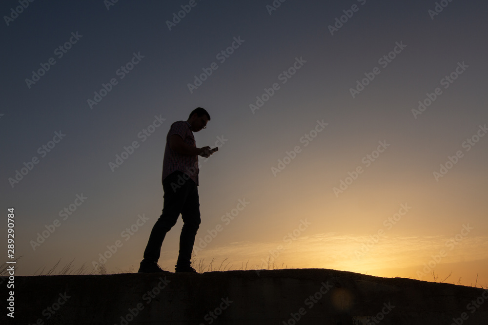 silhouette of man with cell phone at sunset