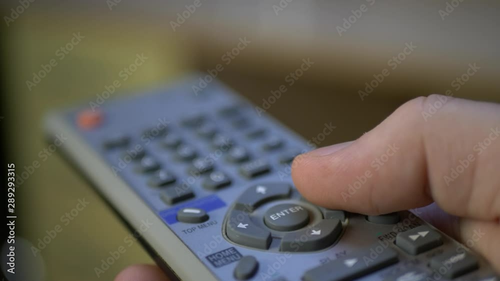 Hand holding silver remote tv controller and push buttons switching channels on TV set Hand holding silver remote tv controller and push buttons switching channels on TV set