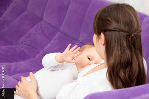 A young woman breast-feeding a baby, sitting on sofa