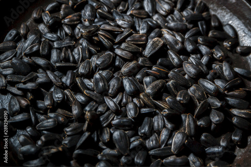 Black fried sunflower seeds in a dark background.