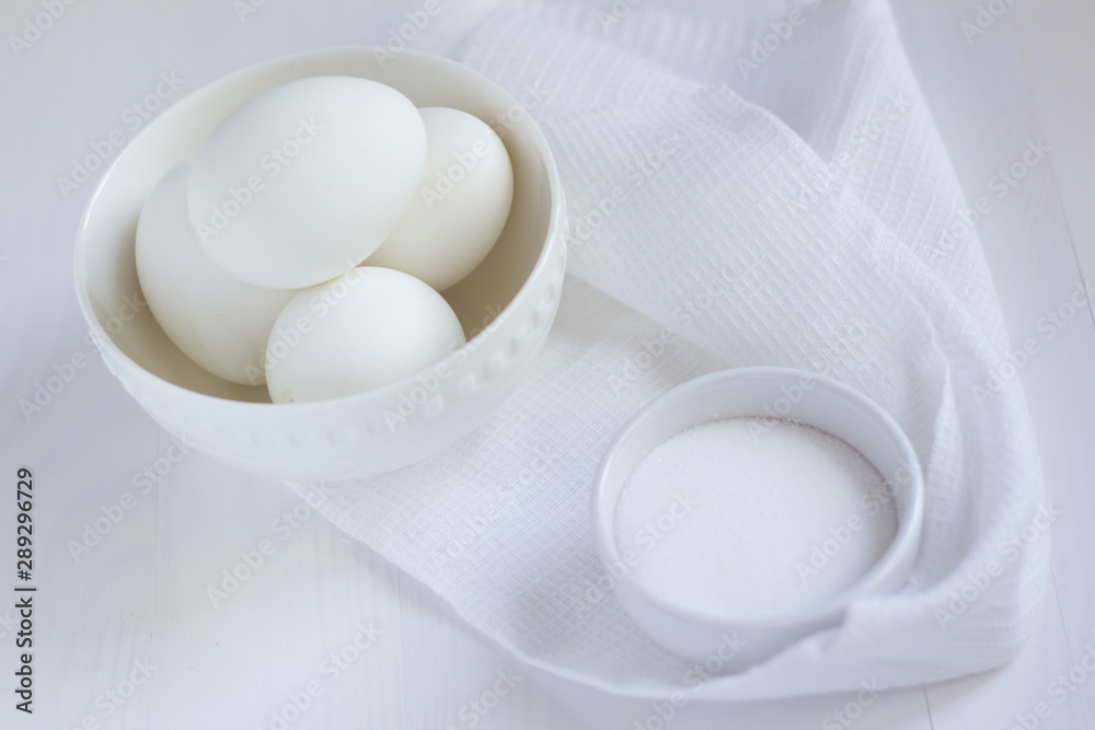 four white eggs lie in a plate on a white wooden table next to a towel and salt shaker. four white eggs lie in a plate on a white wooden table next to a towel and salt shaker.