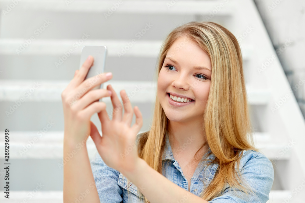 technology and people concept - smiling teenage girl taking selfie by smartphone on stairs