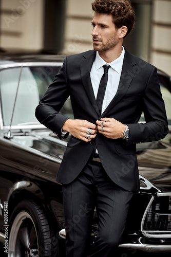 Obraz na płótnie Handsome man with black car wear black suit buttoning his jacket