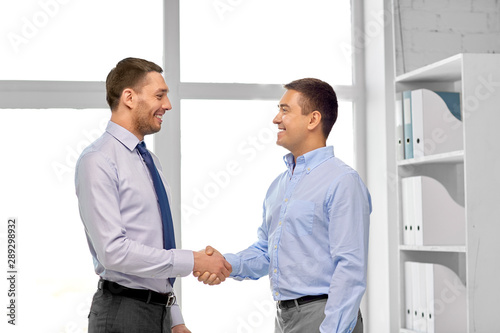 business, gesture and partnership concept - happy businessmen making handshake at office