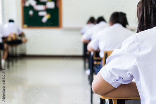 Blurred of behind group of Asian high school, university student having test exams for taking writing examination in school rows chairs at classroom of Thailand. Educational exam assessment Concept