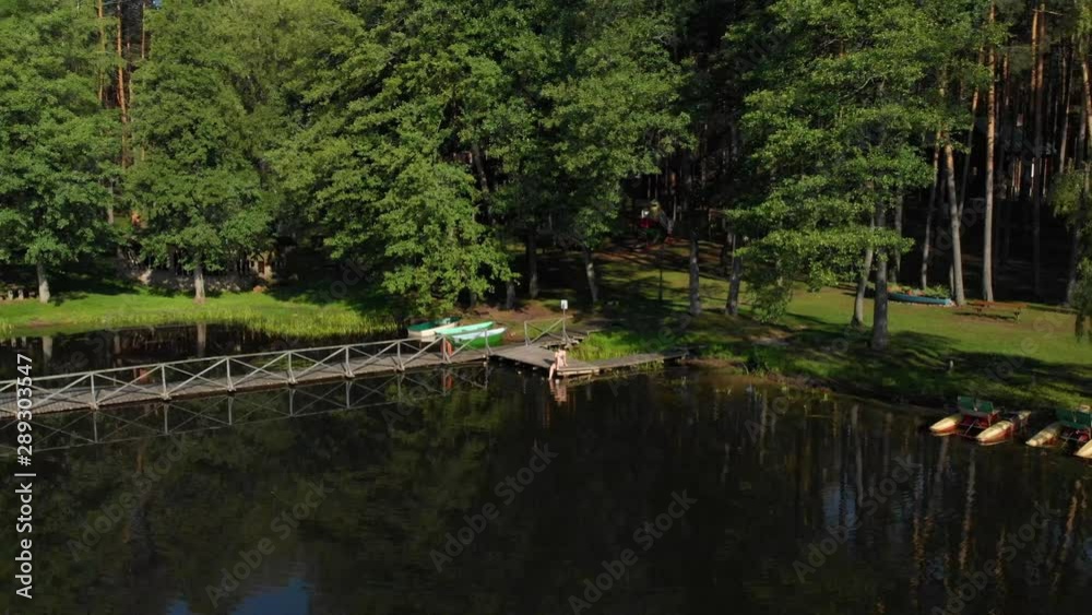 Aerial flying away from people sat enjoying the sun on a wooden boardwalk on Saulys Lake in Lithuania Aerial flying away from people sat enjoying the sun on a wooden boardwalk on Saulys Lake in Lithuania
