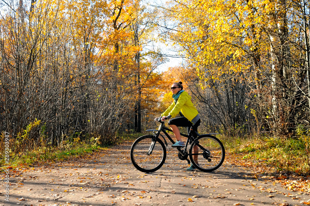 Girl with a bicycle on the road among autumn forest