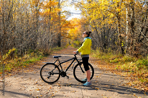 Girl with a bicycle on the road among autumn forest