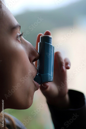 Health and medicine - Young girl using blue asthma inhaler to prevent an asthma attack.