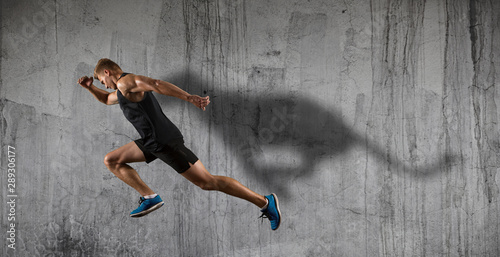 Athletic man sprinter running on dark wall background