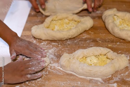 Baker hands preparing khachapuri on kitchen table. A child prepares a traditional Georgian dish - khachapuri with cheese from dough. Culinary, cooking, recipe concept.
